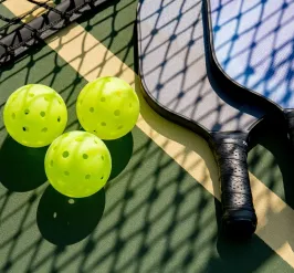 Pickleballs and paddles on the ground on a pickleball court